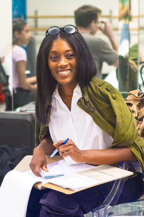 Vicky Lambert smiling with a clipboard of notes, talking with a student in the studio